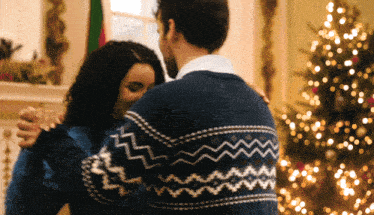 a man in a blue sweater is dancing with a woman in front of a christmas tree