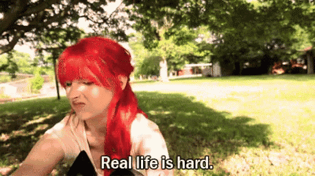 a woman with red hair is sitting in the grass and says real life is hard .