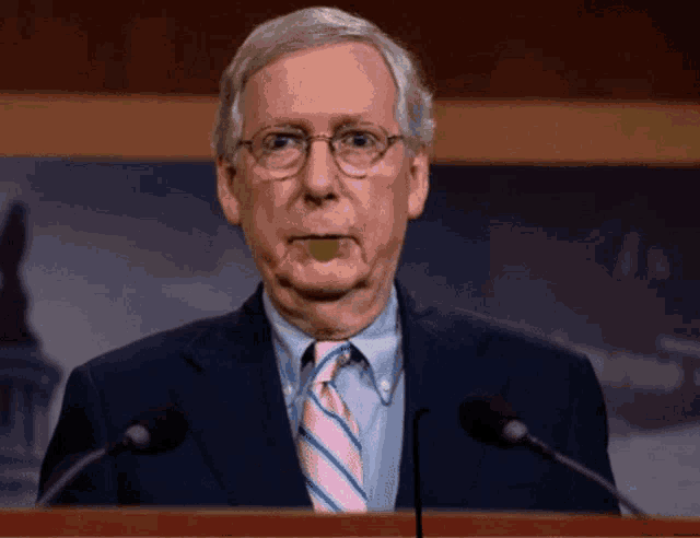 a man with glasses and a pink tie stands at a podium