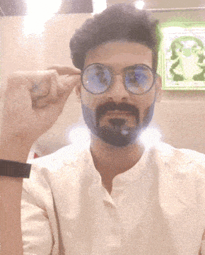 a man with glasses and a beard holds his hand up