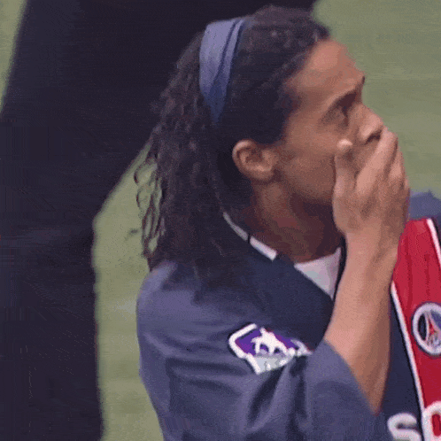 a soccer player covering his mouth with his hand while wearing a headband and a jersey that says psg on it