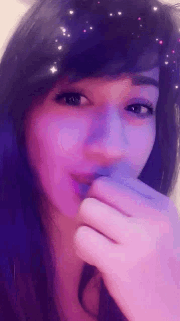 a woman is covering her mouth with her hand while wearing a purple filter .
