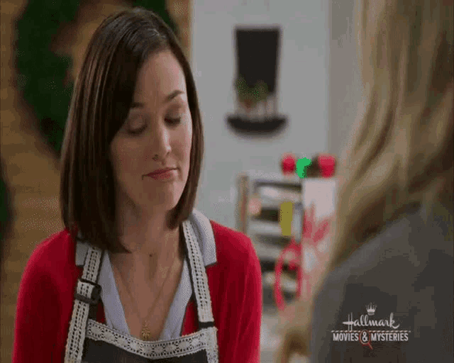a woman wearing an apron is talking to another woman in a hallmark movie .