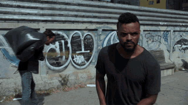a man is standing in front of a wall with graffiti on it including the letters j and o