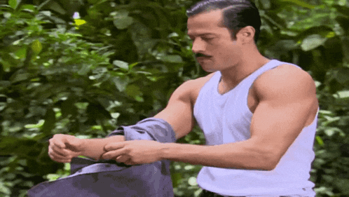 a man in a white tank top with a mustache adjusts his shirt