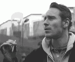 a man is smoking a cigarette in a black and white photo while wearing a hoodie .