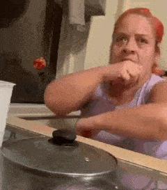 a woman is sitting at a counter with a pot on it and covering her mouth with her hand .