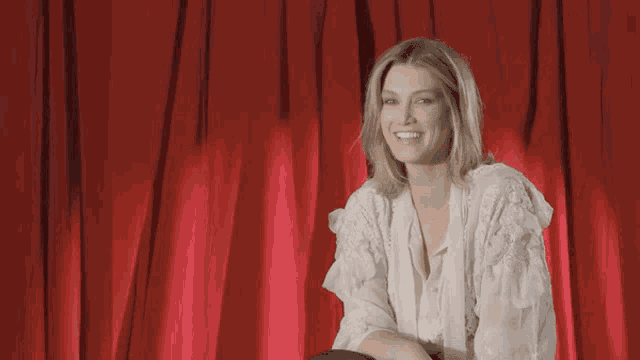 a woman in a white blouse is smiling in front of a red curtain
