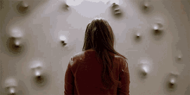 a woman in a red sweater is standing in front of a wall with faces coming out of it