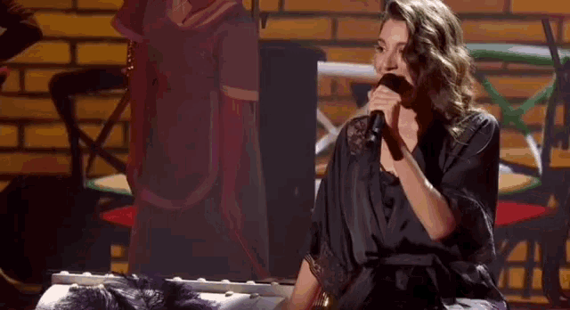 a woman is singing into a microphone while sitting on a piano