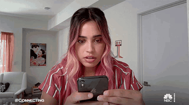 a woman with pink hair is looking at her phone with a nbc logo in the background