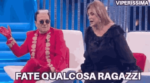 a man in a red suit is sitting next to a woman on a couch and talking to her .