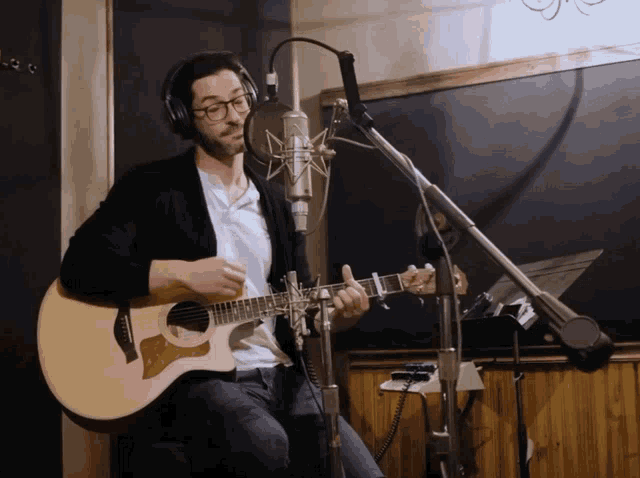 a man wearing headphones is playing an acoustic guitar in front of a microphone