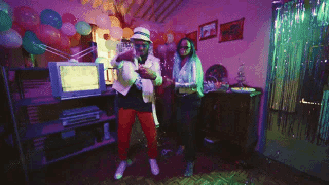 two men are dancing in a room with balloons and a computer monitor