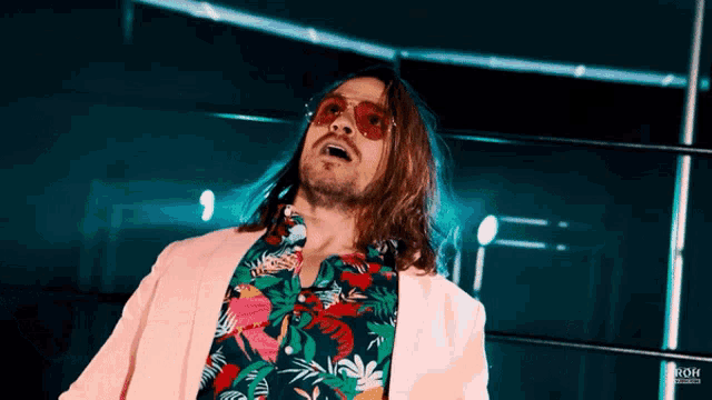 a man with long hair is wearing a pink jacket and a tropical shirt