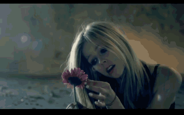 a woman in a black tank top is holding a pink flower