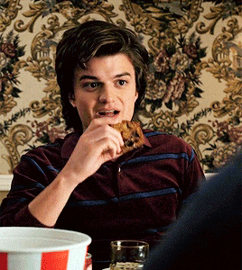 a young man is eating a slice of pizza in front of a floral wallpaper