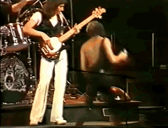 a man is playing a guitar on a stage while another man is kneeling down next to him .