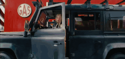 a man is sitting in a car with the door open in front of a gas sign