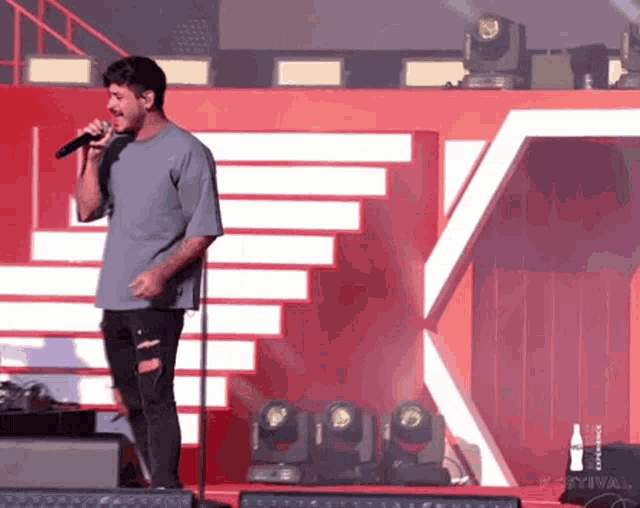 a man is singing into a microphone on a stage with a coca cola logo behind him