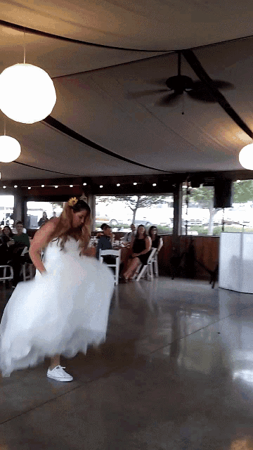 a woman in a wedding dress and white sneakers is dancing on a dance floor