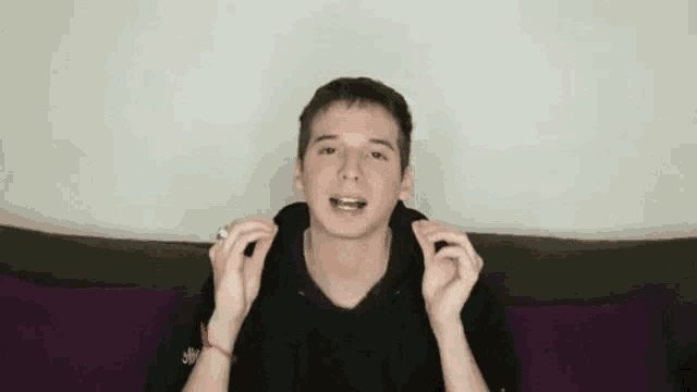 a young man is sitting on a couch with his hands on his ears and making a funny face .