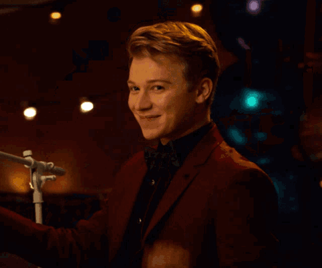 a young man in a red suit and bow tie waves his hand in front of a microphone