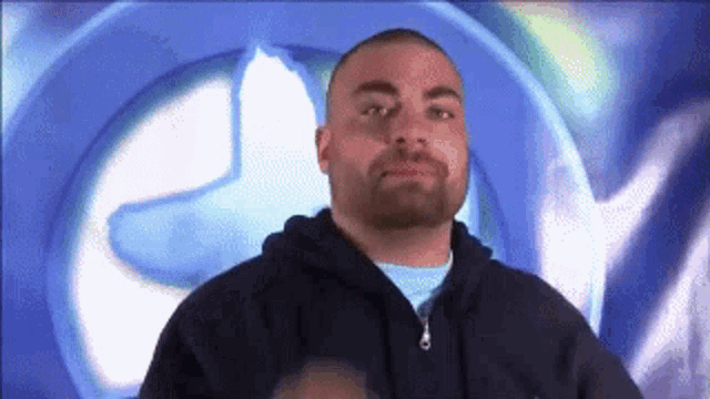 a man with a beard is standing in front of a blue circle with the letter c on it