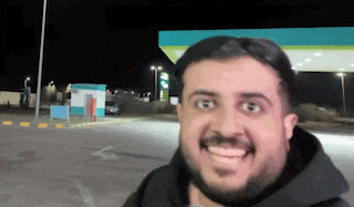 a man with a beard is smiling in front of a petrol station