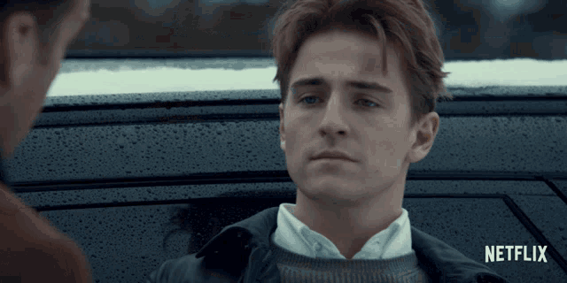 a man is sitting in a car with a netflix logo behind him