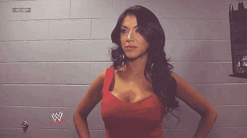 a woman in a red dress is standing in front of a brick wall with a w logo on it .