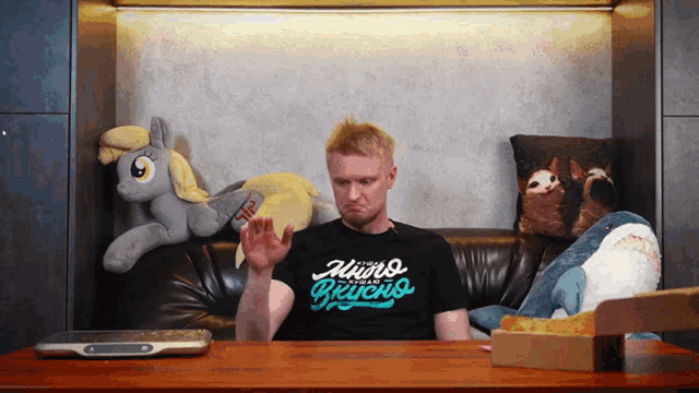 a man sitting on a couch with stuffed animals wearing a shirt that says " hurd psycho " on it