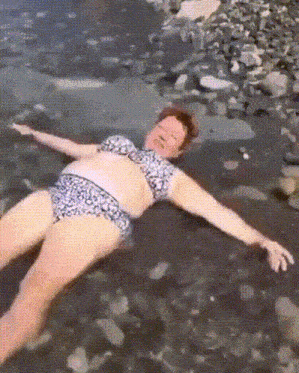 a woman in a bikini is laying on a rocky beach with her arms outstretched .