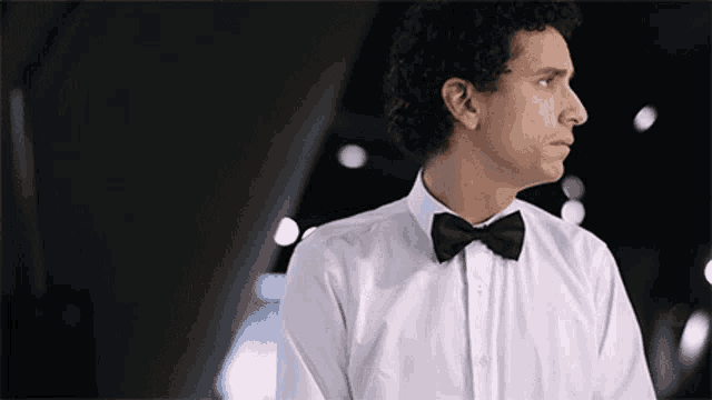 a man in a white shirt and black bow tie looks to the side