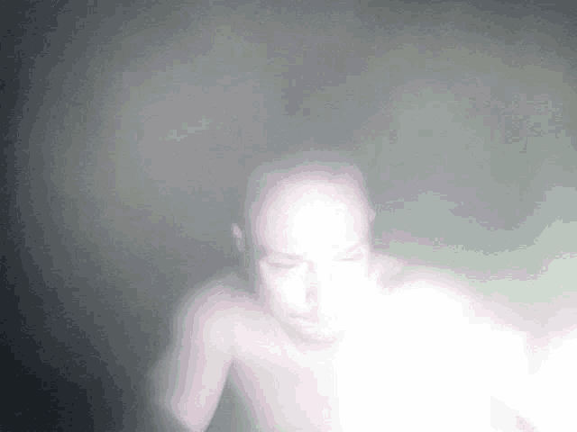 a man without a shirt is standing in a dark room with a light shining on him .