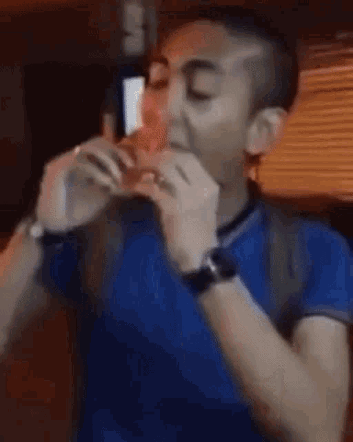 a man in a blue shirt is eating a hamburger while wearing a watch .