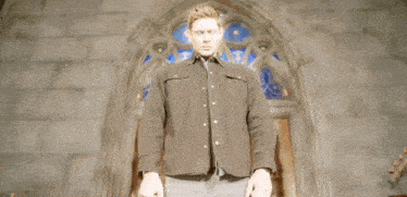 a man in a brown jacket is standing in front of a church