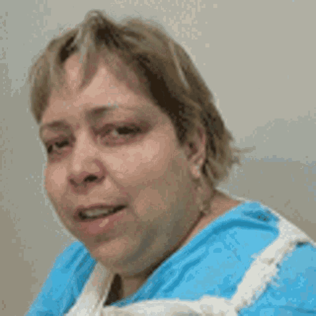 a woman in a blue shirt and apron is smiling for the camera .