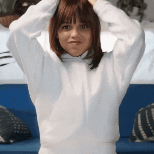 a woman in a white sweatshirt is holding her hair