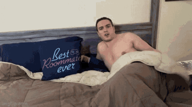 a shirtless man is laying on a bed next to a pillow that says best roommate ever