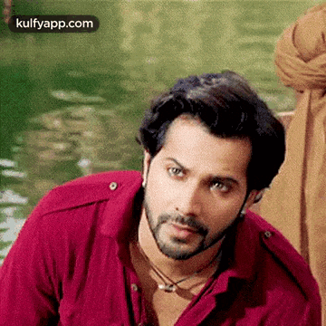 a man with a beard and a red shirt is looking at the camera .