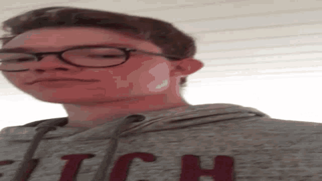 a young man wearing glasses and a gray hoodie is looking down at the camera .