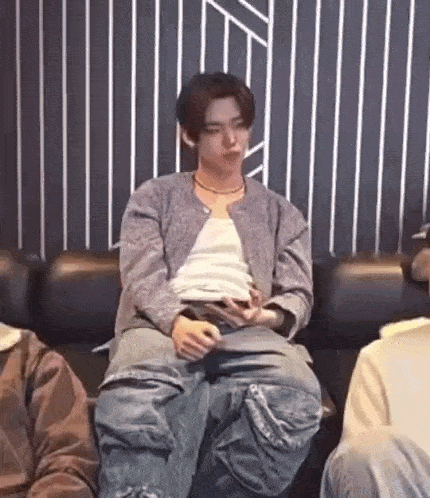 a man is sitting on a couch with his legs crossed while holding a cell phone .