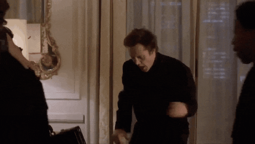 a man in a black suit is standing in a room talking to a woman .