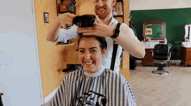 a man is cutting a woman 's hair in a barber shop with a striped cape that says rick on it