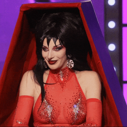 a woman in a red top and gloves is in a purple coffin