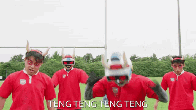 a group of men wearing red shirts and horned helmets are dancing in a field with the words teng teng teng teng below them