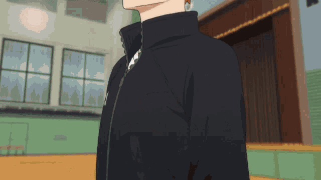 a man in a black jacket is standing in a room with a green wall .
