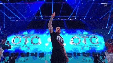a man is standing on a stage with his hand in the air in front of a sign that says oto oto
