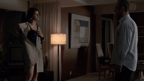 a man in a blue shirt is standing in a room with a lamp